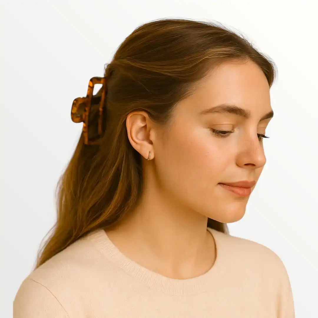 Een vrouw met een tortoise shell haarklem, een lichtkleurig lange mouwen topje en kleine hoop oorbellen.