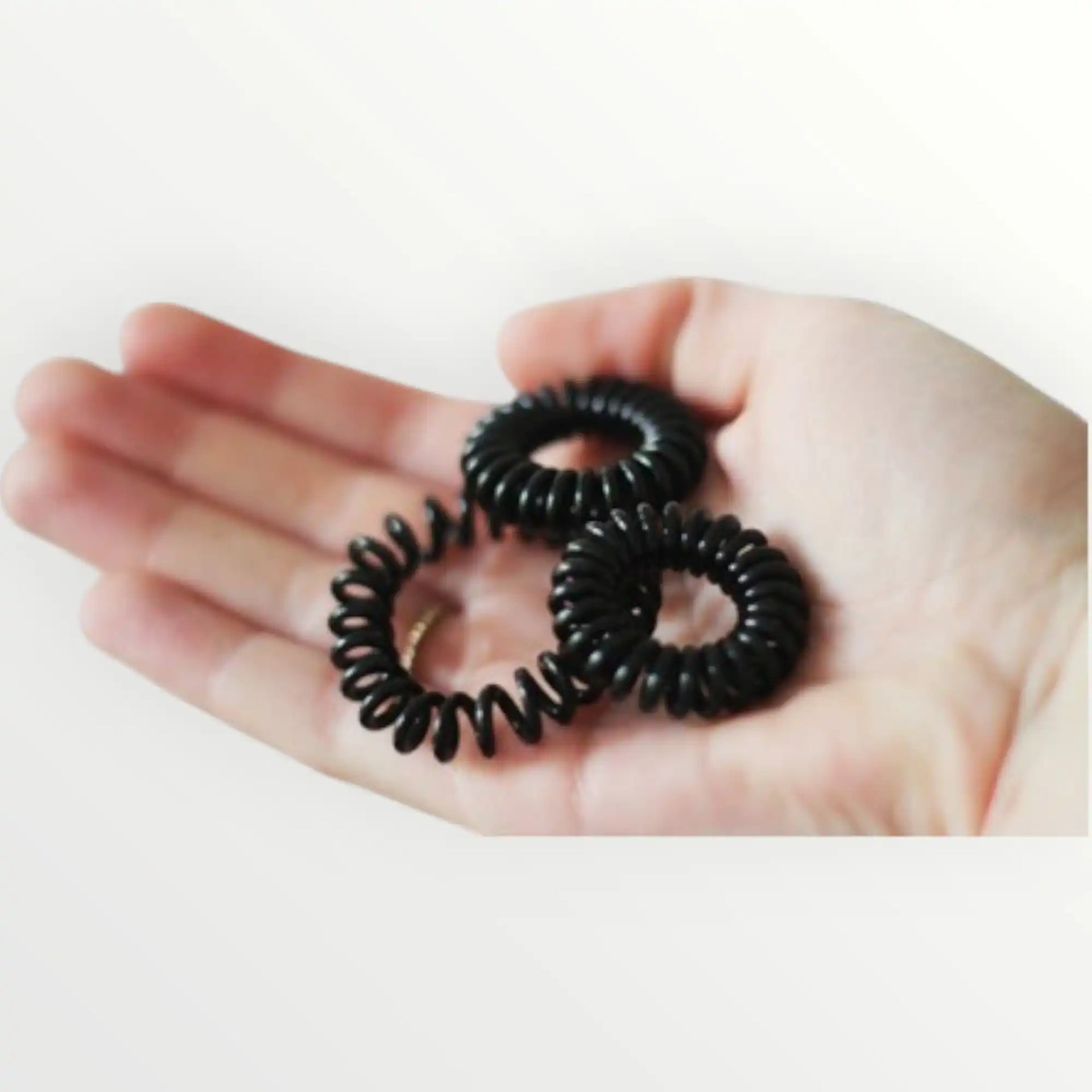 Drie zwarte spiraalhaarbandjes in de open hand van een persoon.