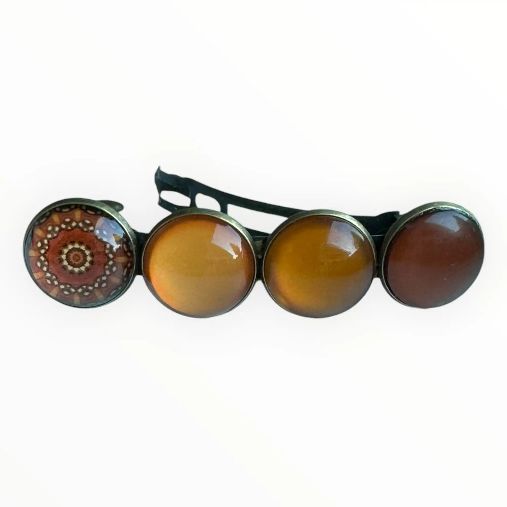 Een haarspeld met vier ronde cabochons, waarvan één met een rood en oranje mandalapatroon en drie in verschillende tinten amber en bruin.