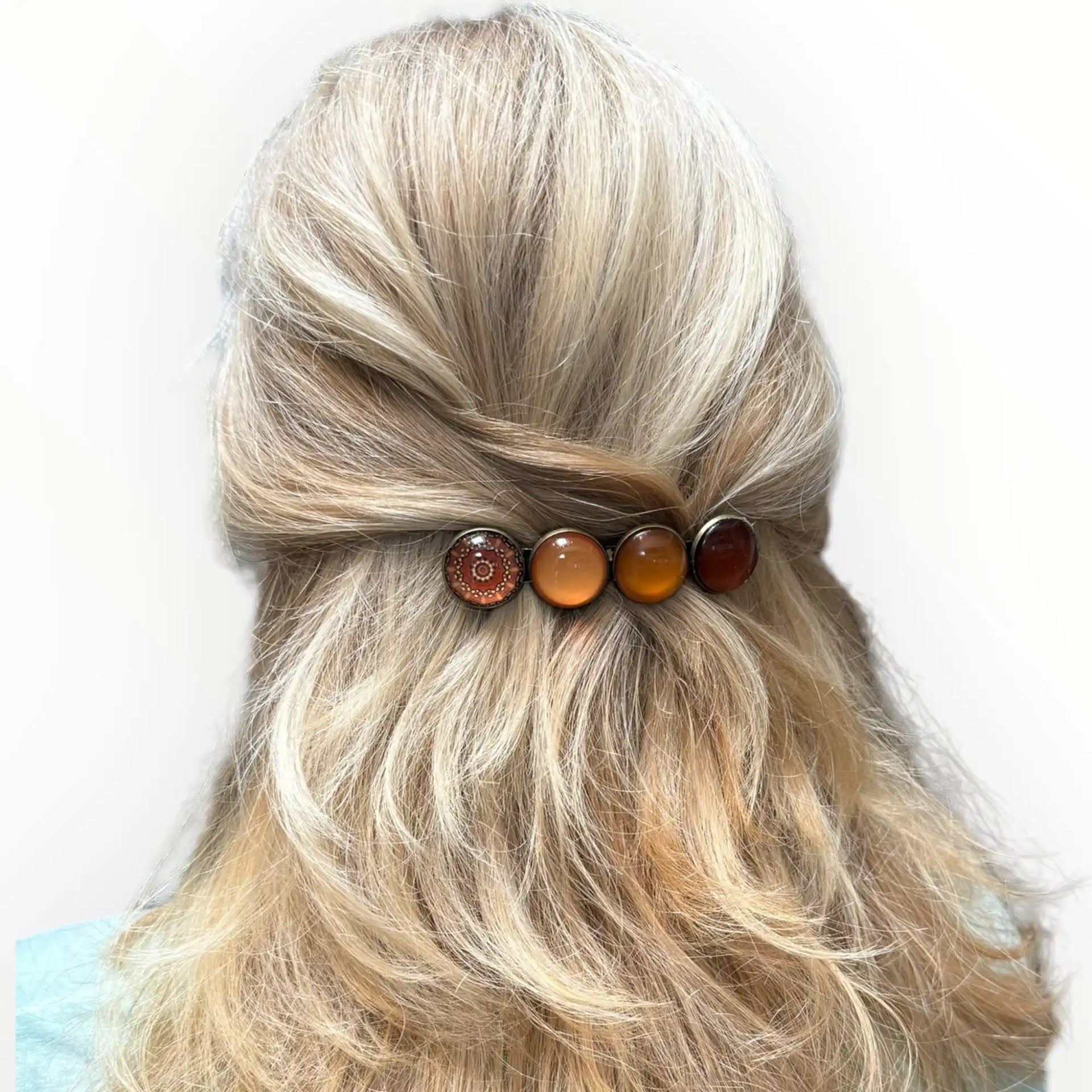 Het haar van een vrouw in een half opgestoken stijl met een decoratieve haarspeld met vier ronde, amberkleurige versieringen.