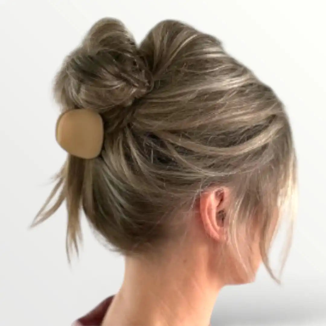 Het haar van een vrouw in een rommelige blonde knot met een lichte bruine haarclip